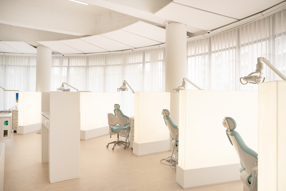 Open-plan treatment area at Milk Orthodontics with softly lit partitions and sheer curtains